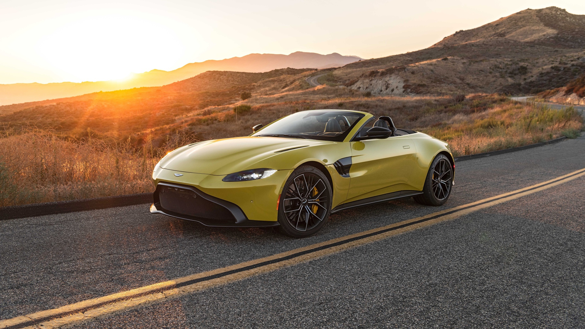 Желтый кабриолет  Aston Martin Vantage Roadster, 2021 года на трассе на рассвете