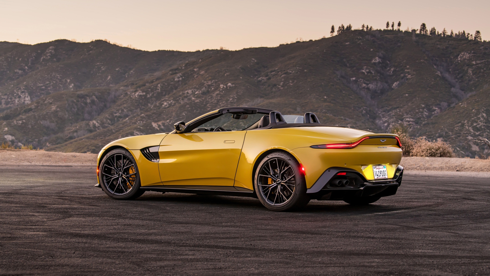 Желтый автомобиль  Aston Martin Vantage Roadster, 2021 года на фоне гор 