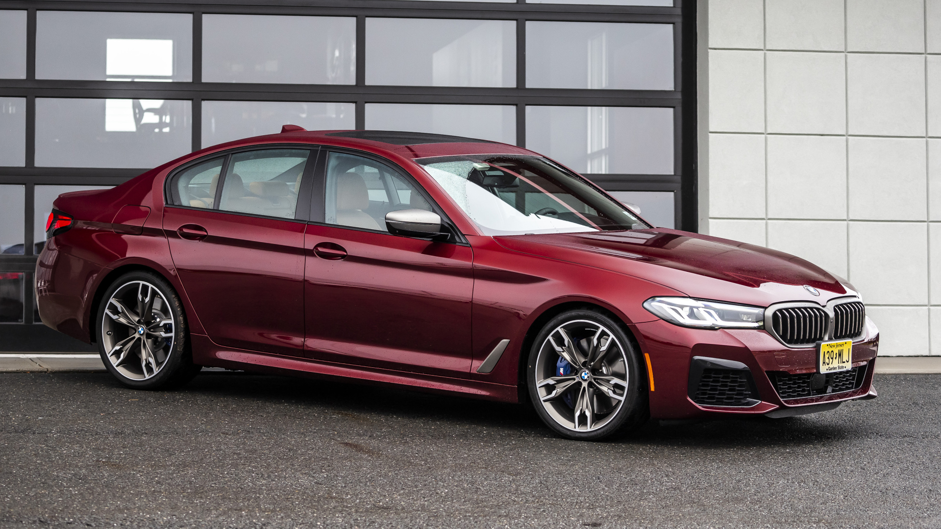 Красный автомобиль BMW M550i XDrive, 2021 года у гаража