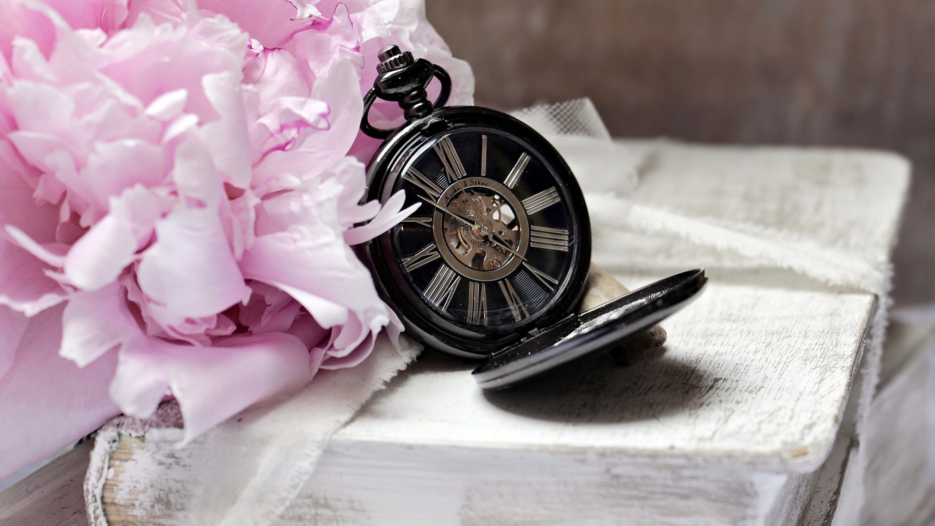 Черные карманные часы с книгой и цветами на столе 