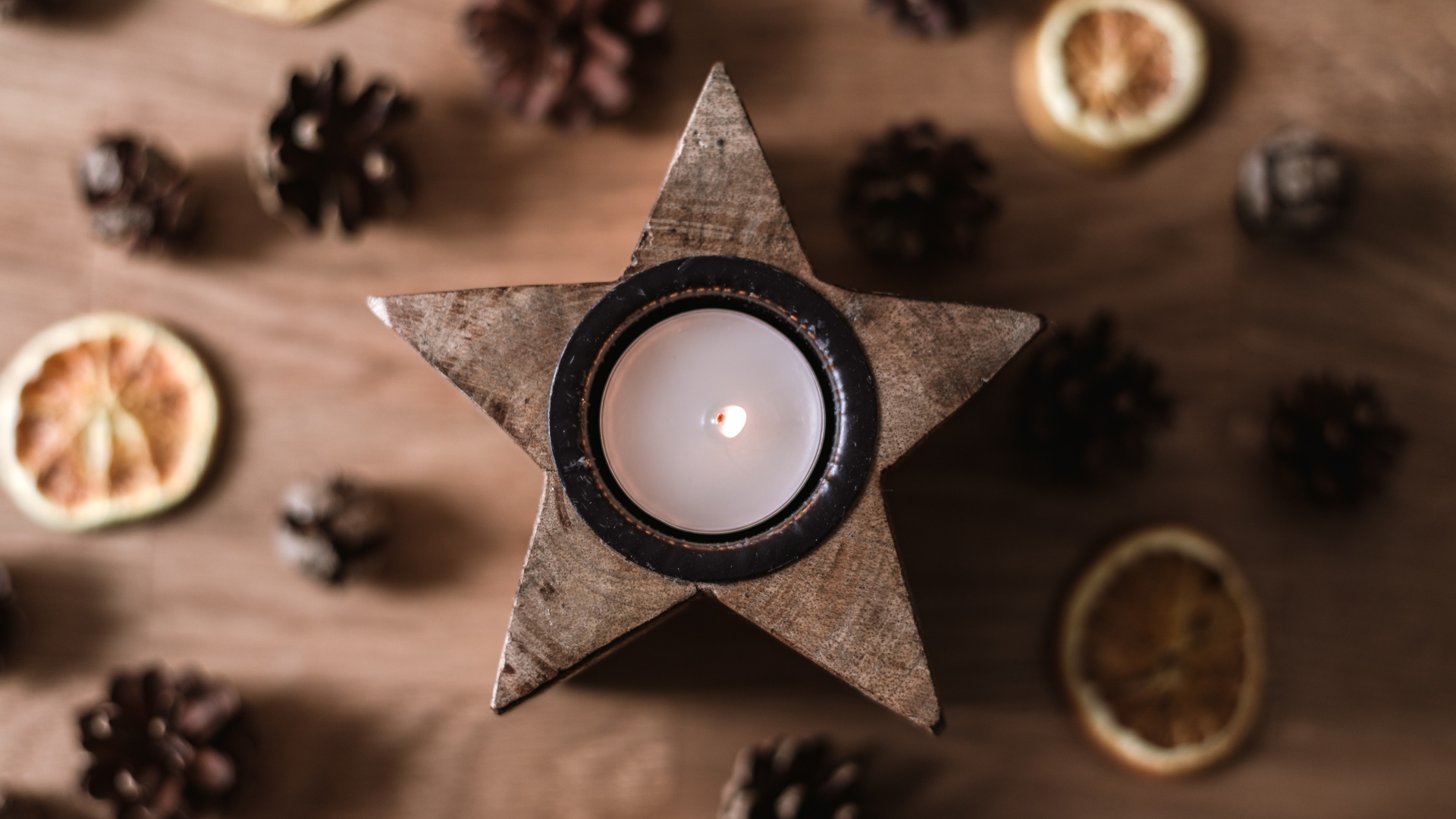 Свеча в форме звезды на столе с шишками и сушеным апельсином