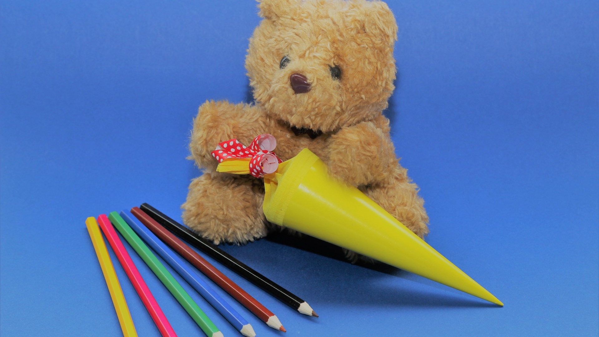 Игрушечный медвежонок  с карандашами на синем фоне