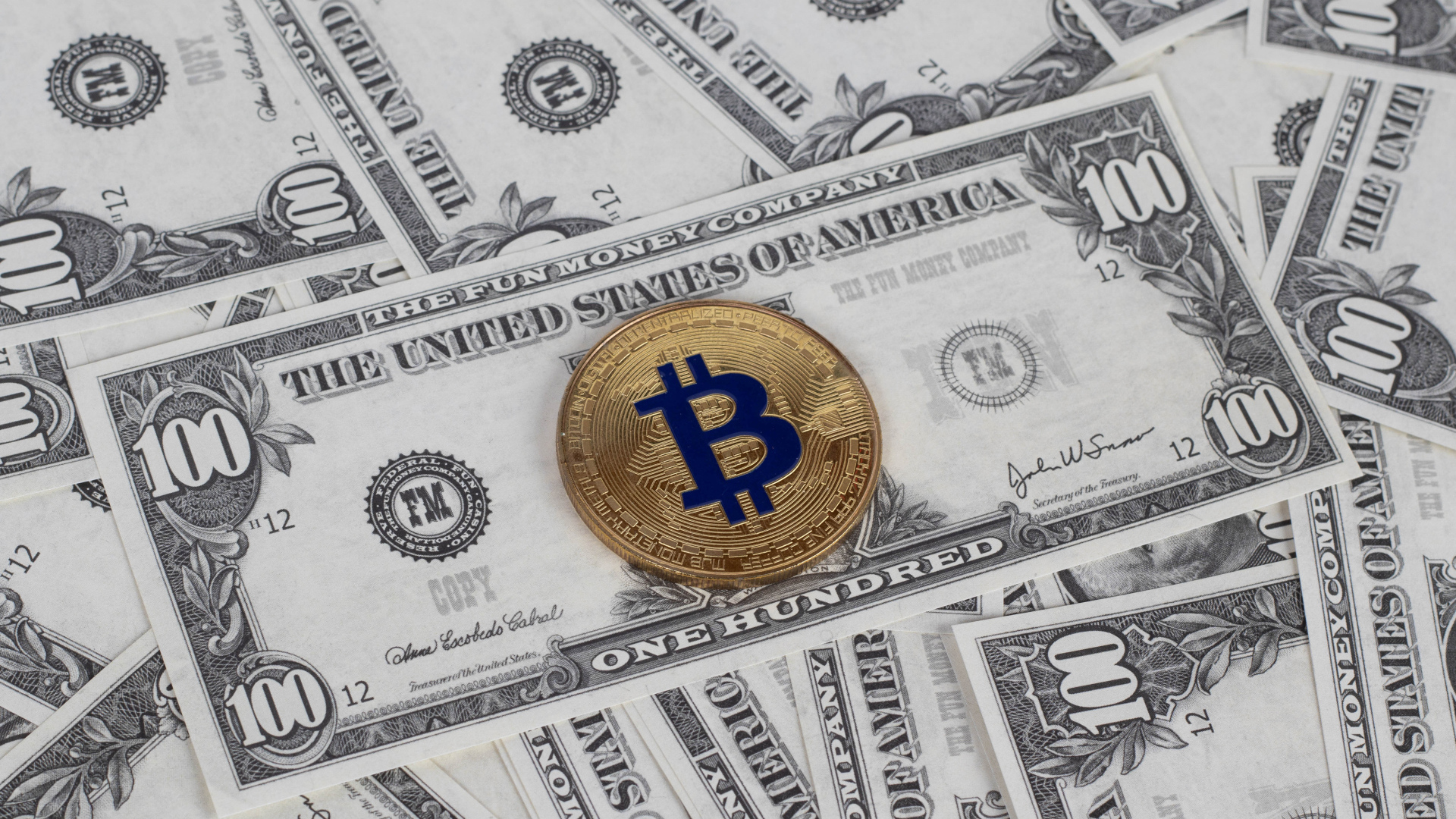 Монета Биткоин лежит на стодолларовых купюрах