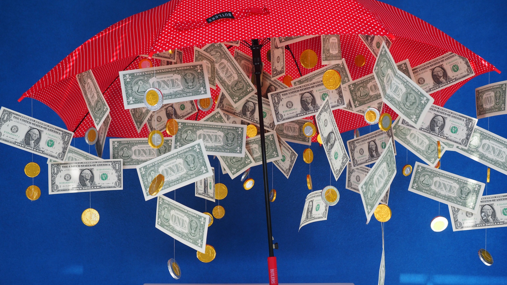 Доллары и монеты высыпаются из зонта на голубом фоне