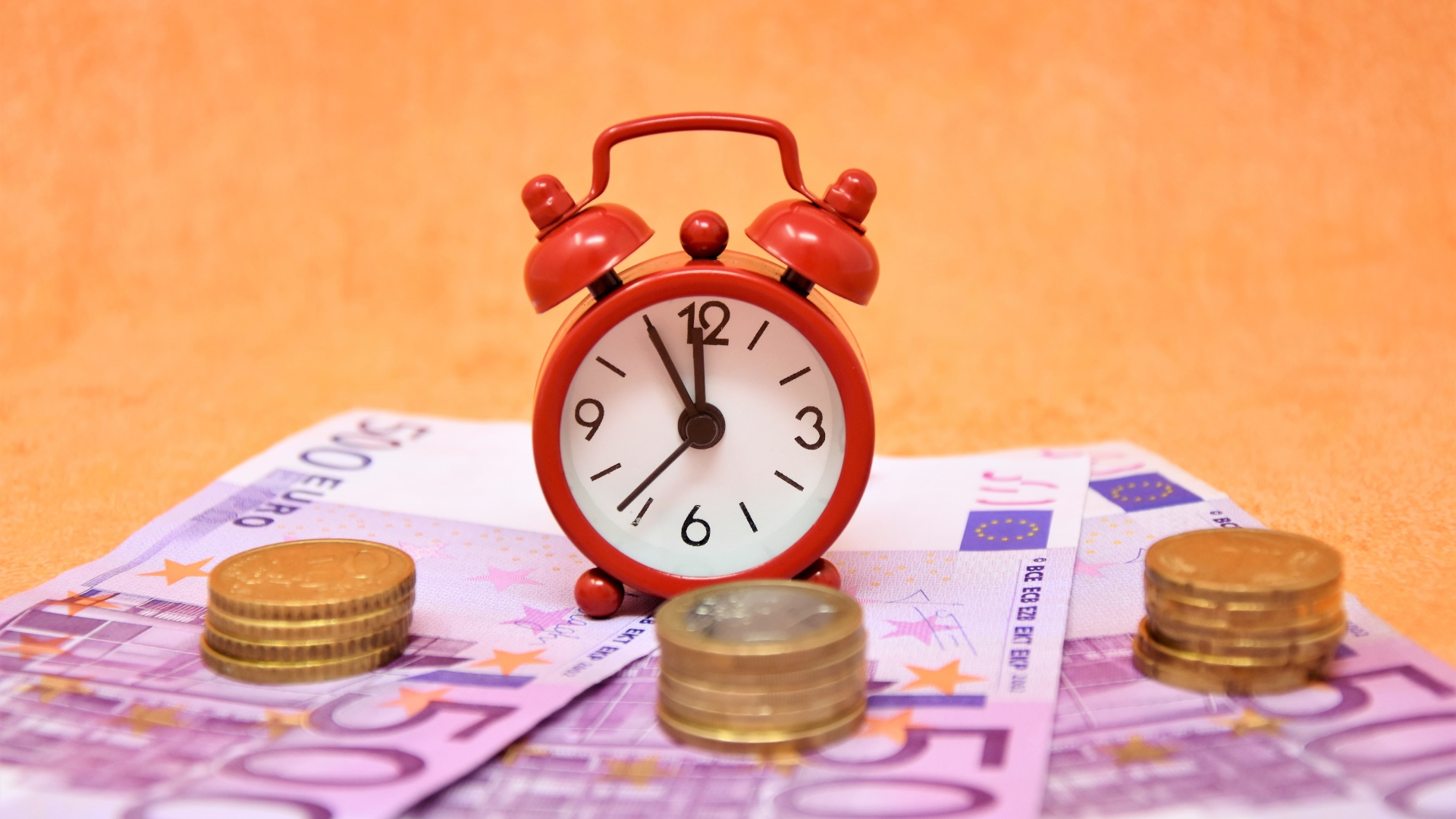 Маленький красный будильник с купюрами евро и монетами