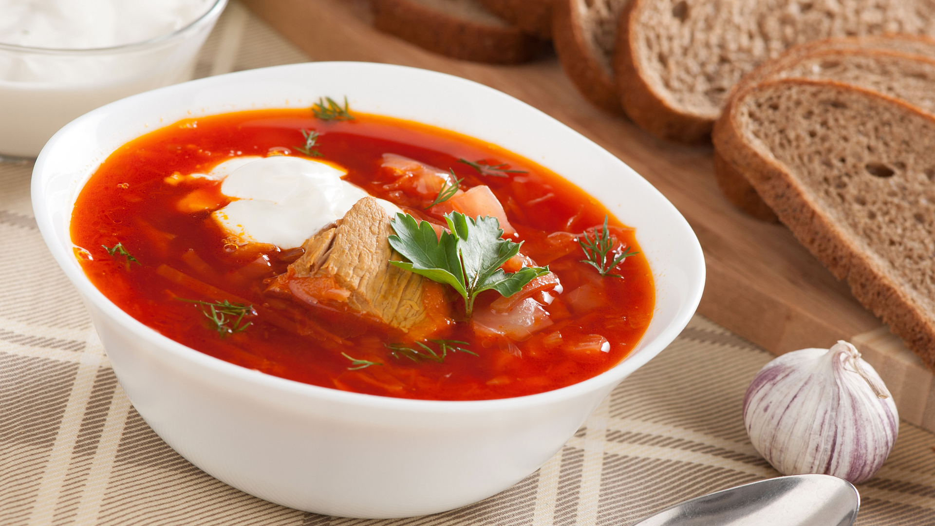 Тарелка горячего борща на столе с хлебом и чесноком