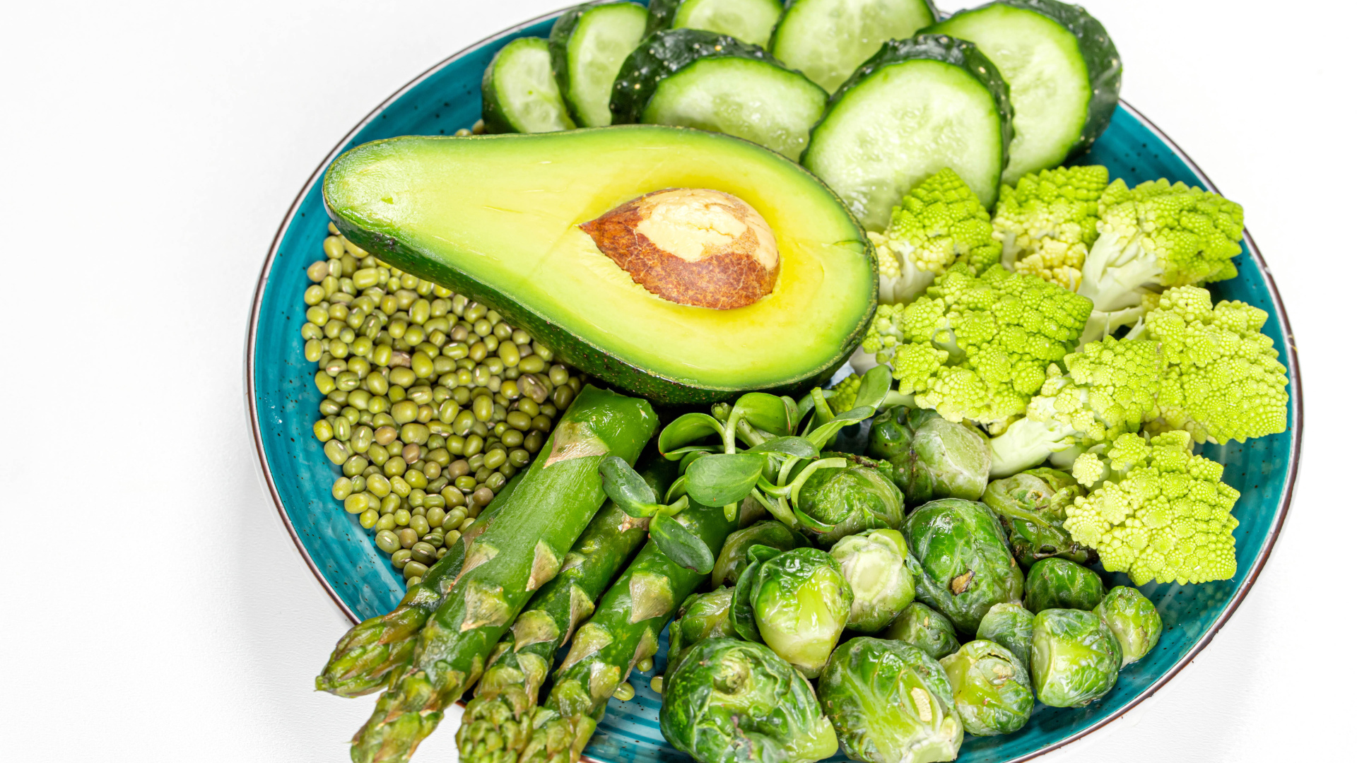 Авокадо, капуста, огурцы и спаржа на тарелке на белом фоне