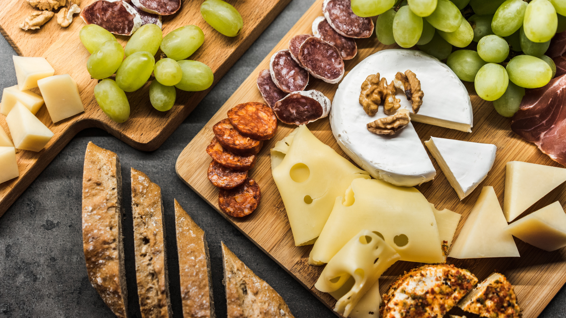 Сыр, колбаса, виноград и батон  на столе 