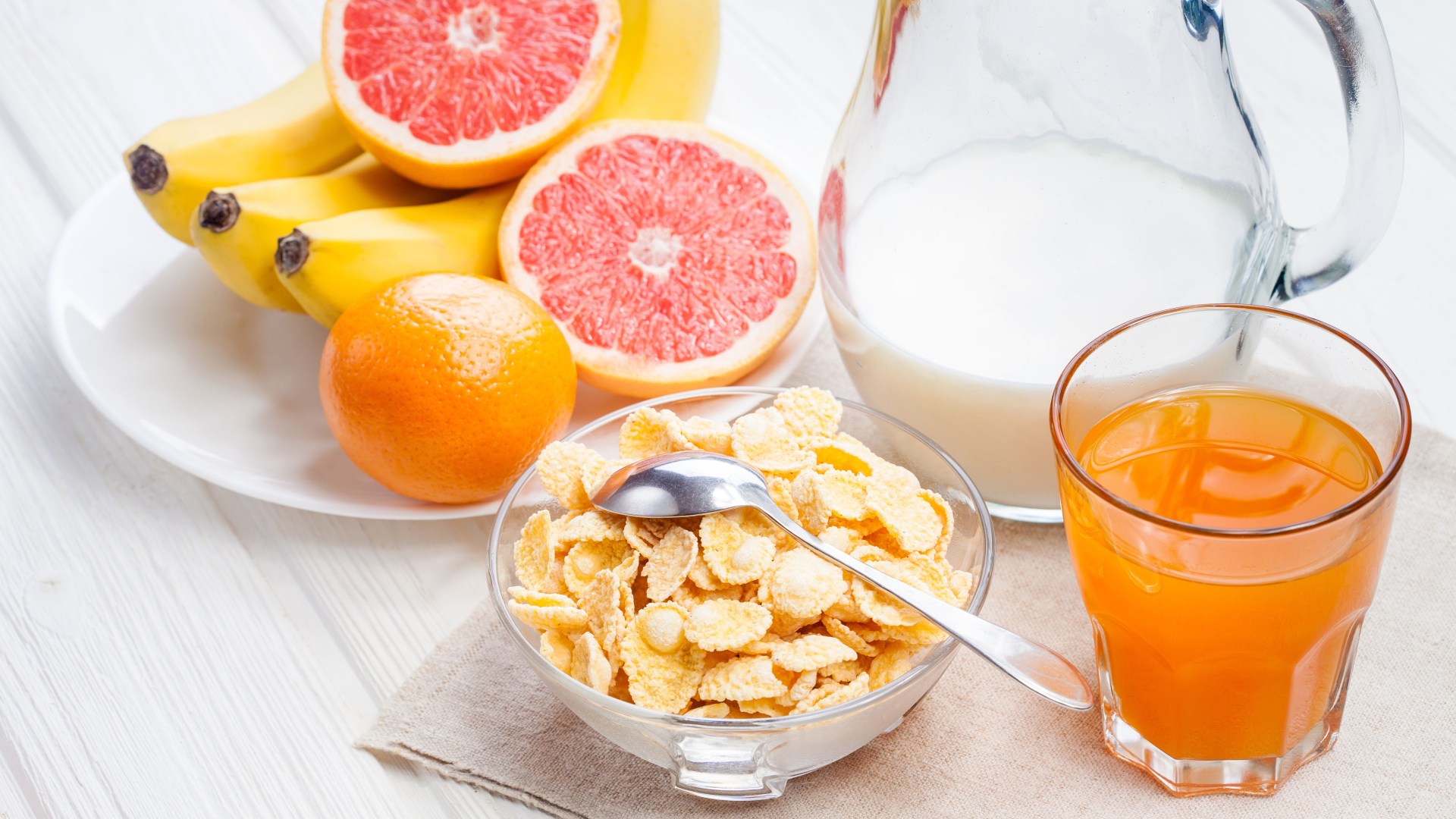 Кукурузные хлопья на столе с молоком, соком и свежими фруктами на завтрак