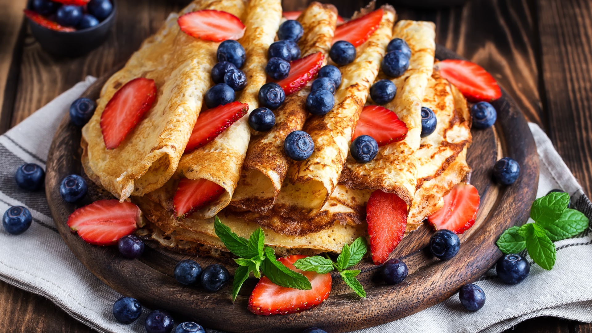 Вкусные тонкие блинчики на деревянной доске с ягодами черники и клубники 