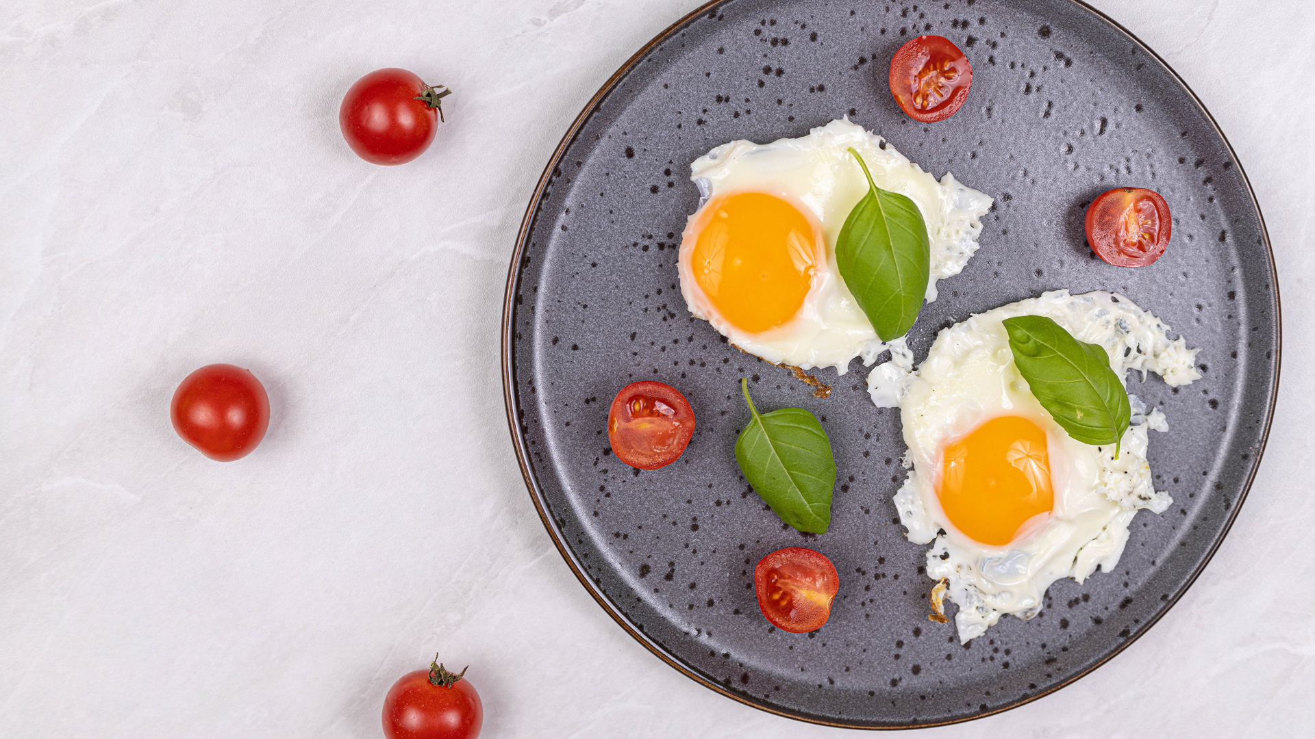 Яичница глазунья с помидорами и листьями базилика на черной тарелке 