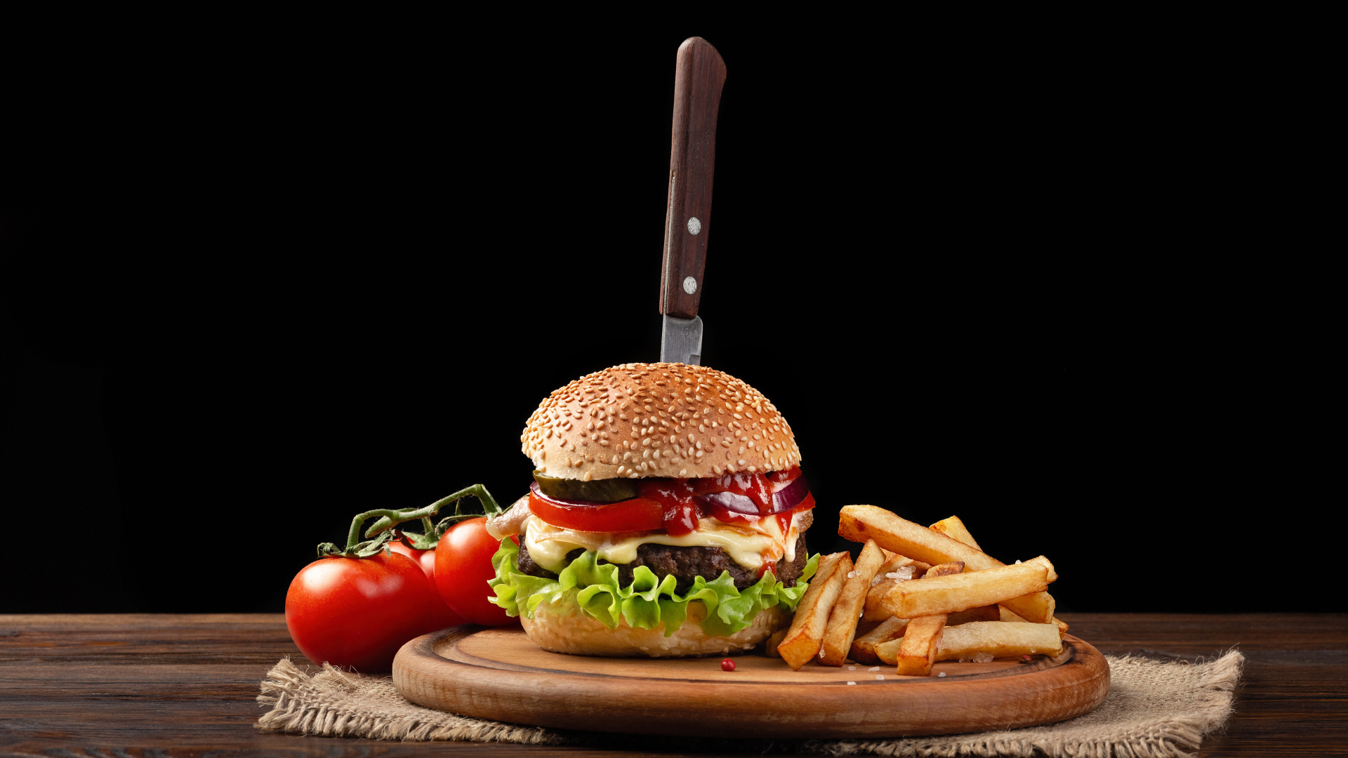 Hamburger with a knife on the table with tomatoes and fries