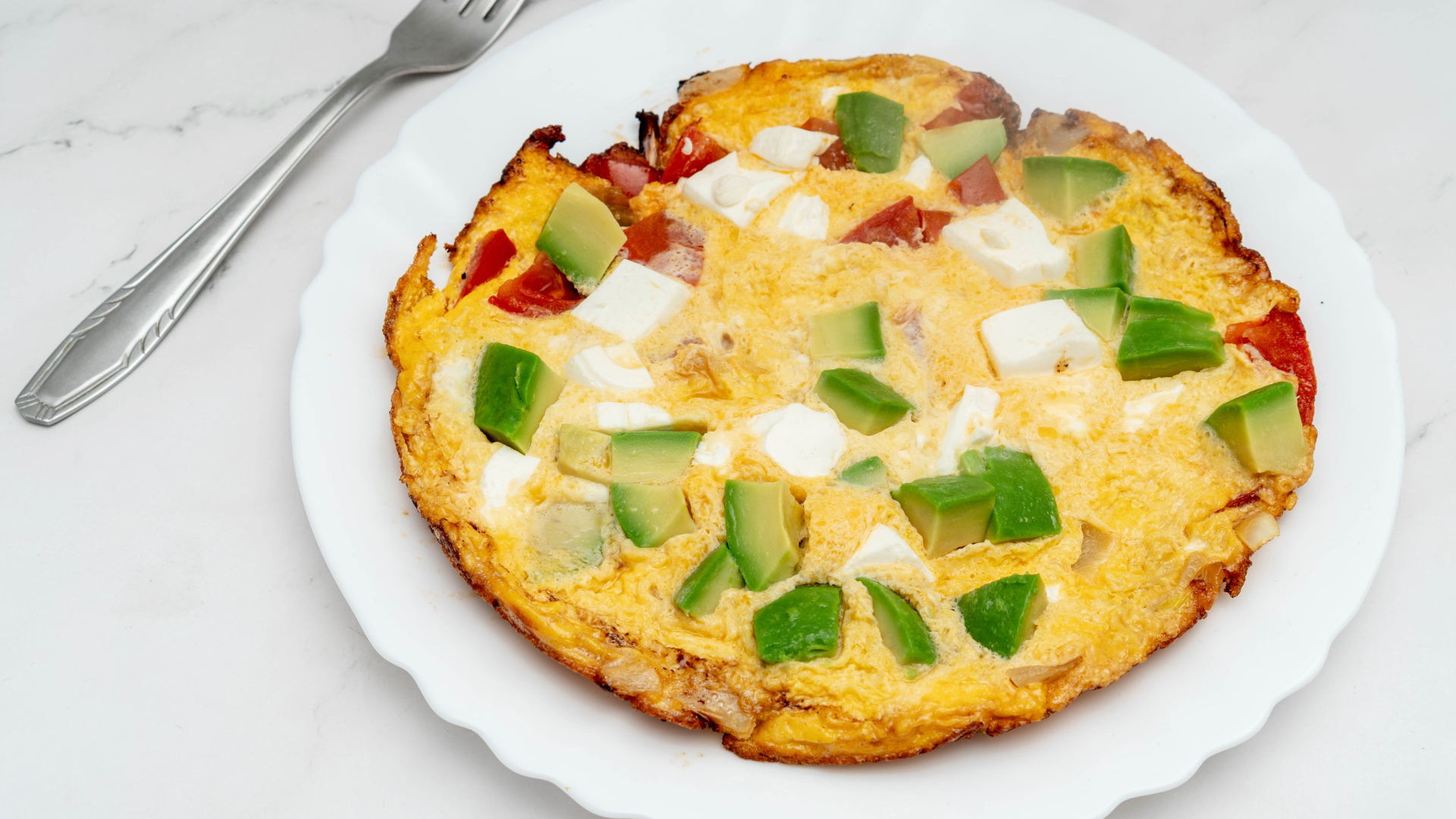 Омлет с авокадо и кусочками помидора на белой тарелке 