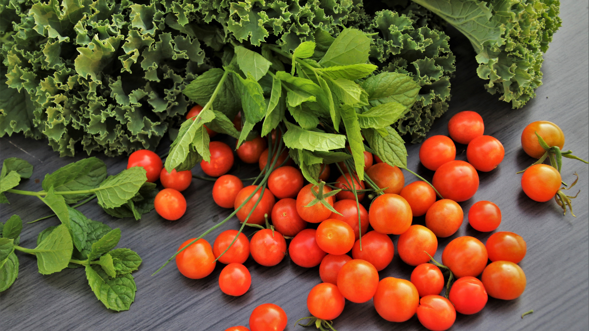 Красные мелкие помидоры на столе с зеленью 