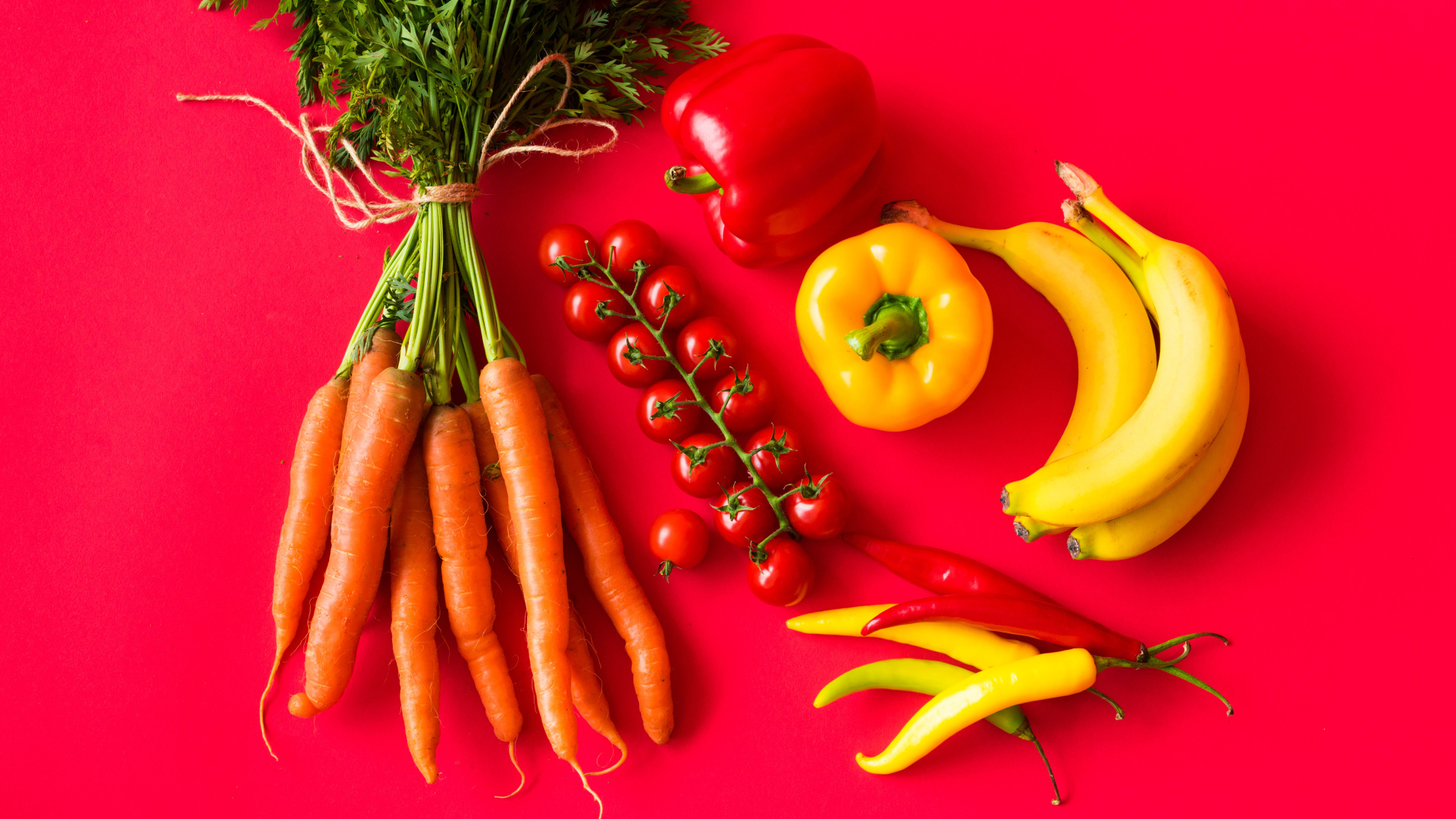 Свежие морковь, помидоры, перец и бананы на красном фоне