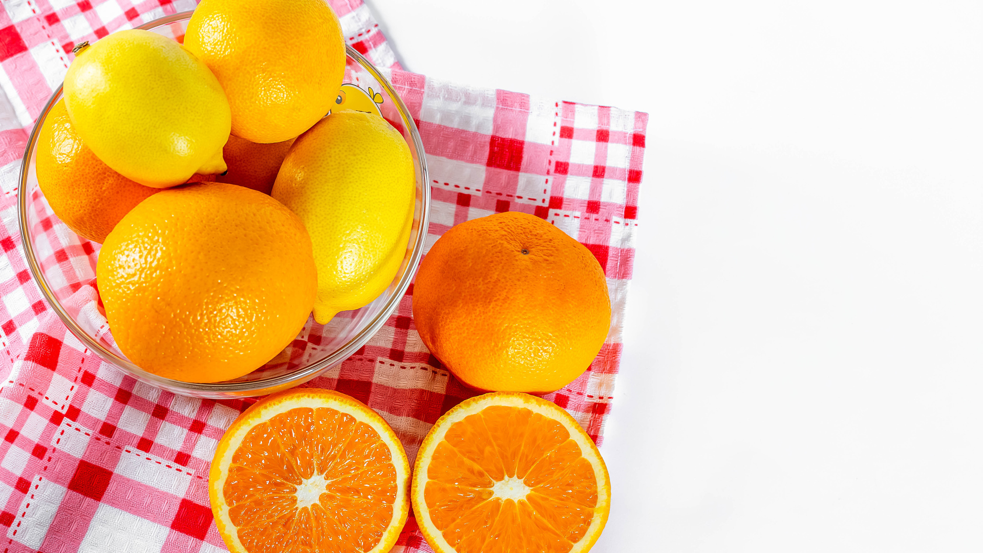 Спелые апельсины и лимоны в стеклянной миске на столе