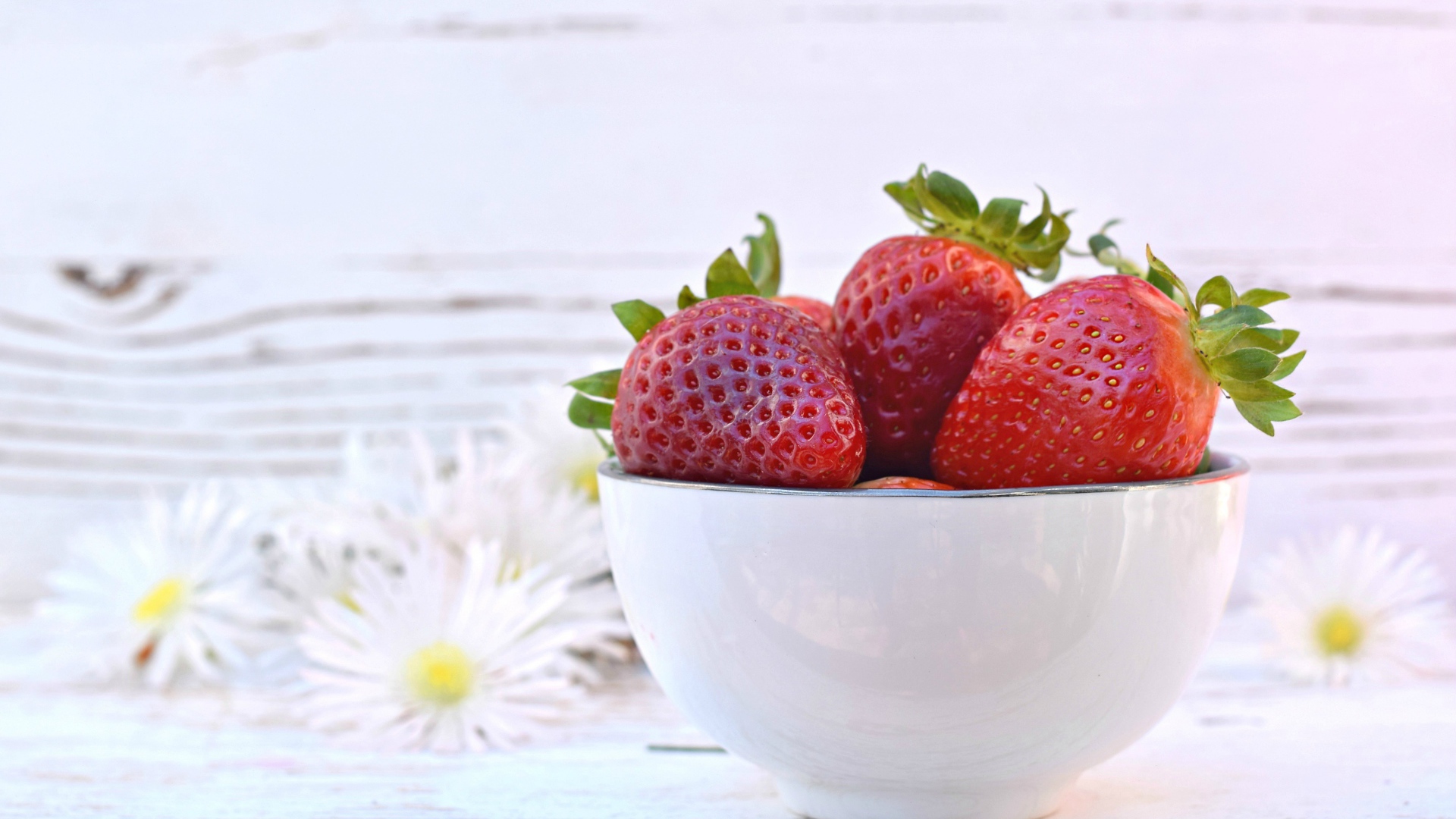 Спелая клубника в белой миске на столе с ромашками