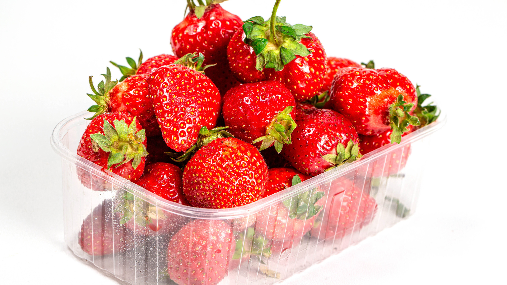 Спелая вкусная клубника в пластиковом контейнере на белом фоне