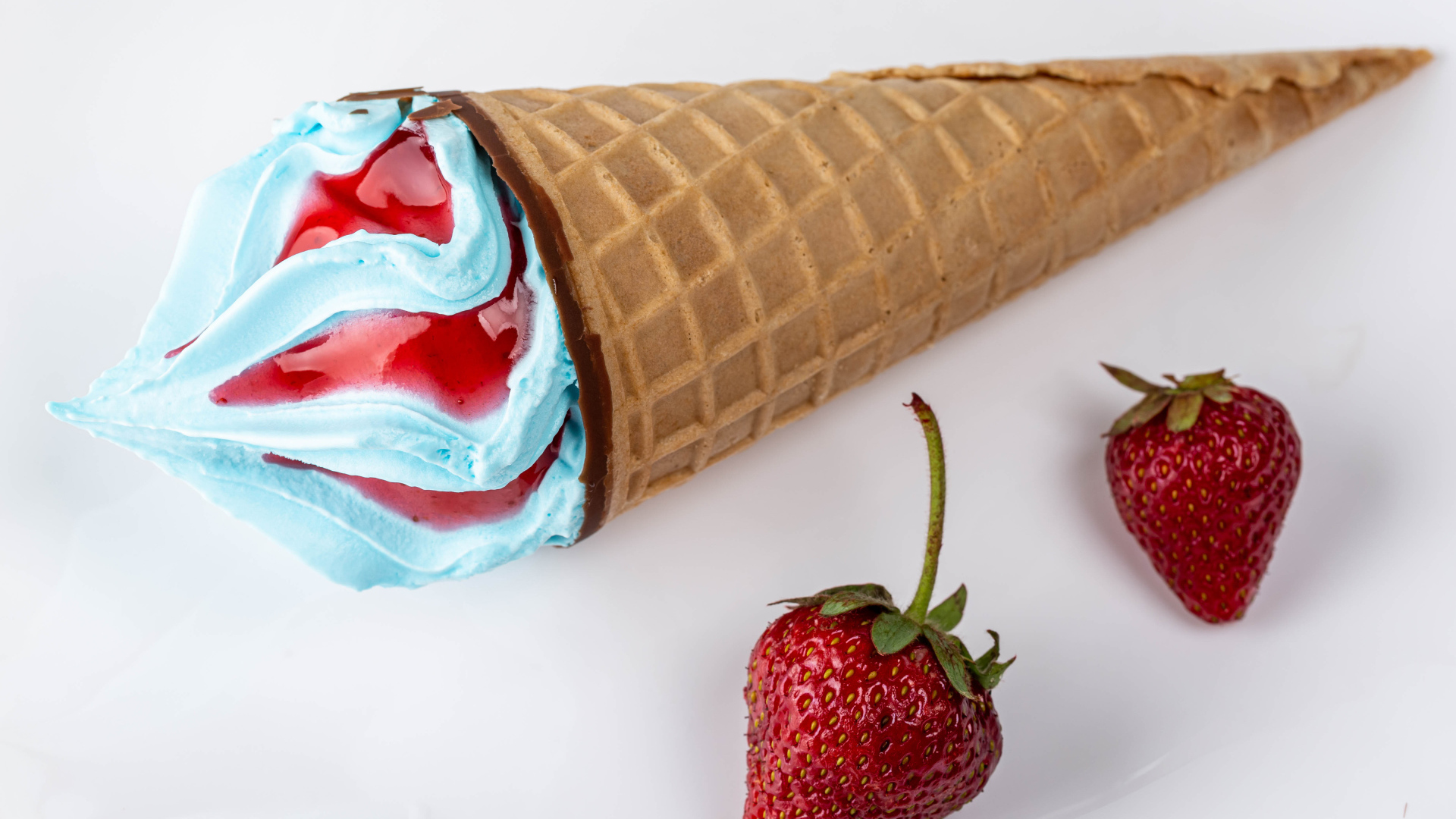 Рожок с голубым мороженым на сером фоне с клубникой 