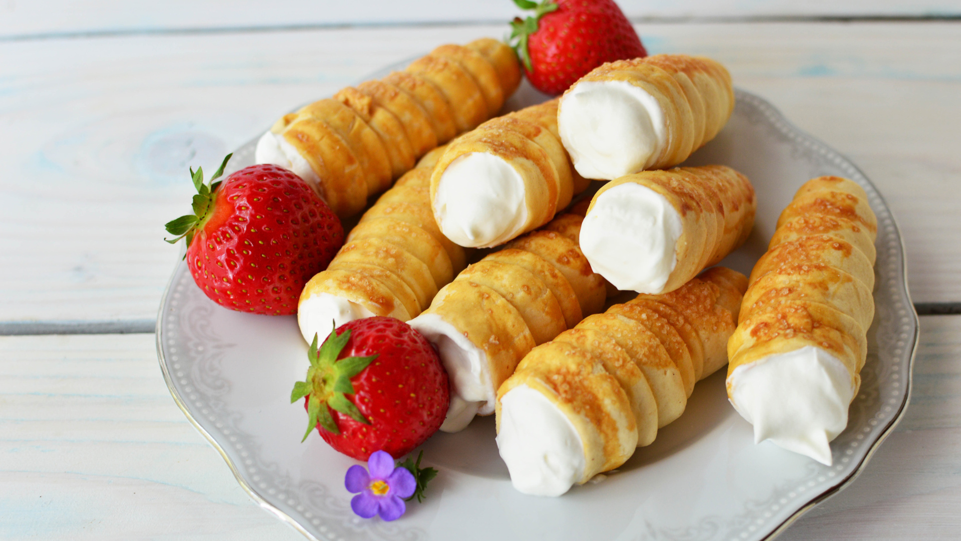 Пирожные трубочки с кремом и ягодами клубники на тарелке 