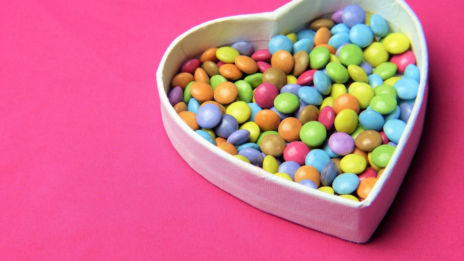 Коробка в форме сердца с разноцветными конфетами на розовом фоне
