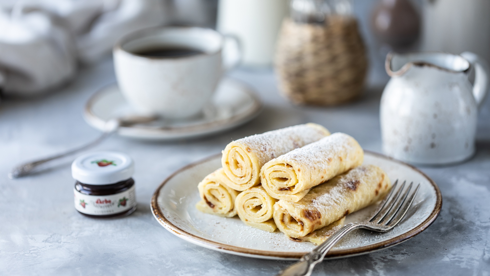 Блины на тарелке с сахарной пудрой на столе с кофе