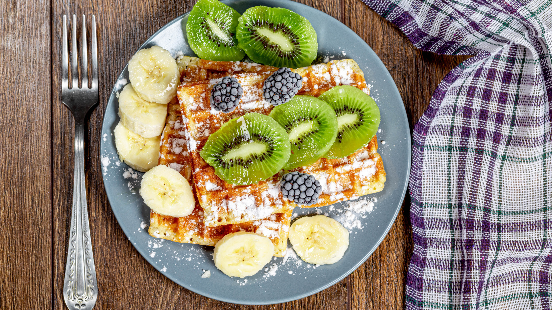 Сладкие вафли на тарелке с сахарной пудрой, бананами и киви