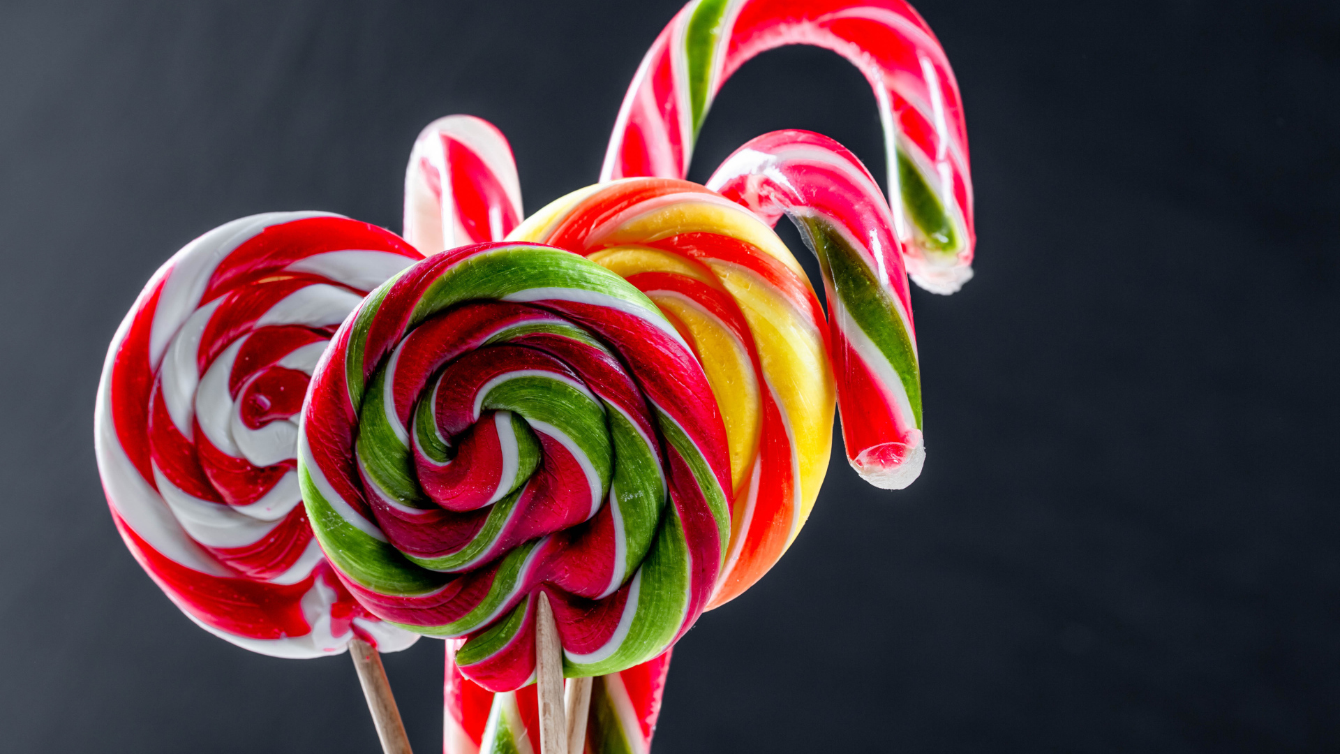 Вкусные разноцветные конфеты на палочке на сером фоне