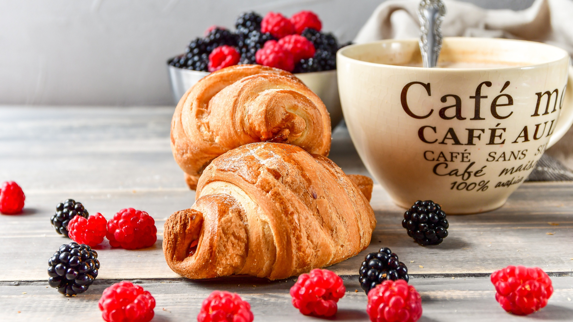 Два круассана с малиной, черникой и чашкой кофе на столе