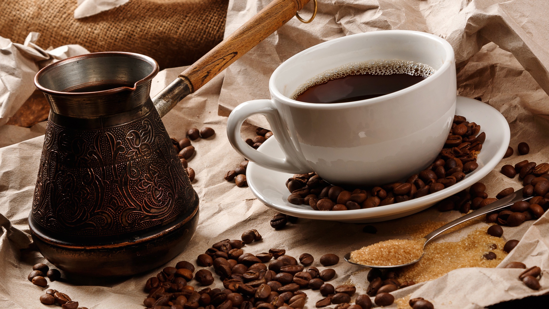 Чашка горячего кофе на столе с туркой, зернами и коричневым сахаром