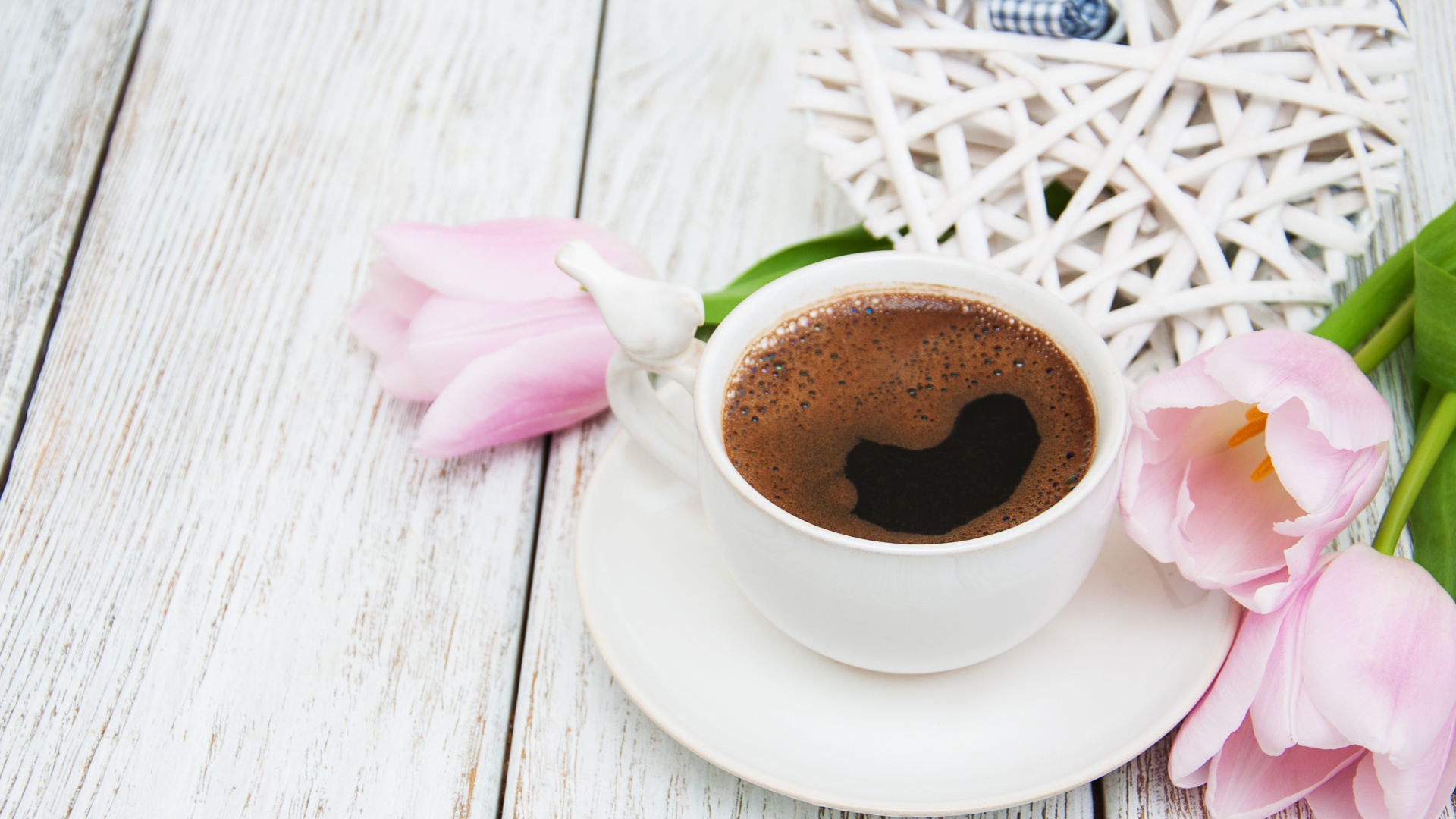 Чашка кофе на столе с розовыми тюльпанами и плетеным сердцем