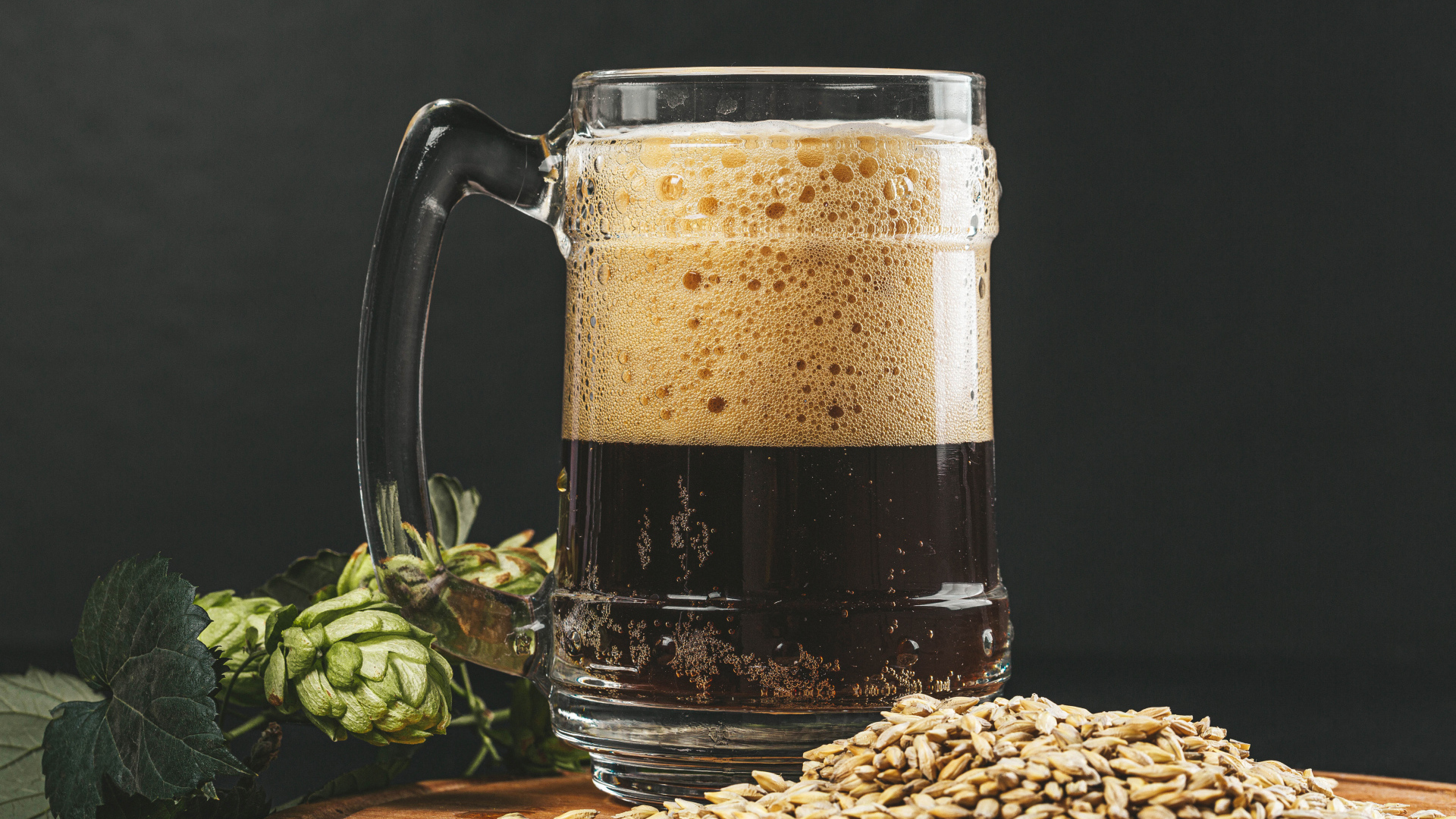 Темное пиво в бокале на столе с хмелем и зернами пшеницы 