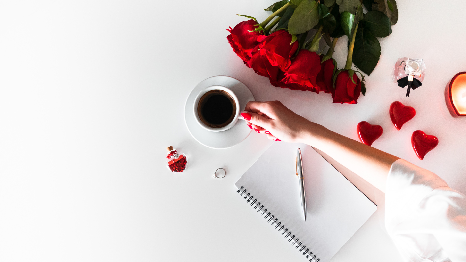 Девушка держит в руках чашку кофе на столе с блокнотом и букетом роз 