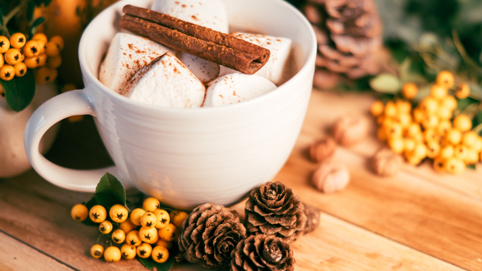 Маршмеллоу в чашке с корицей на столе с шишками и гроздьями рябины