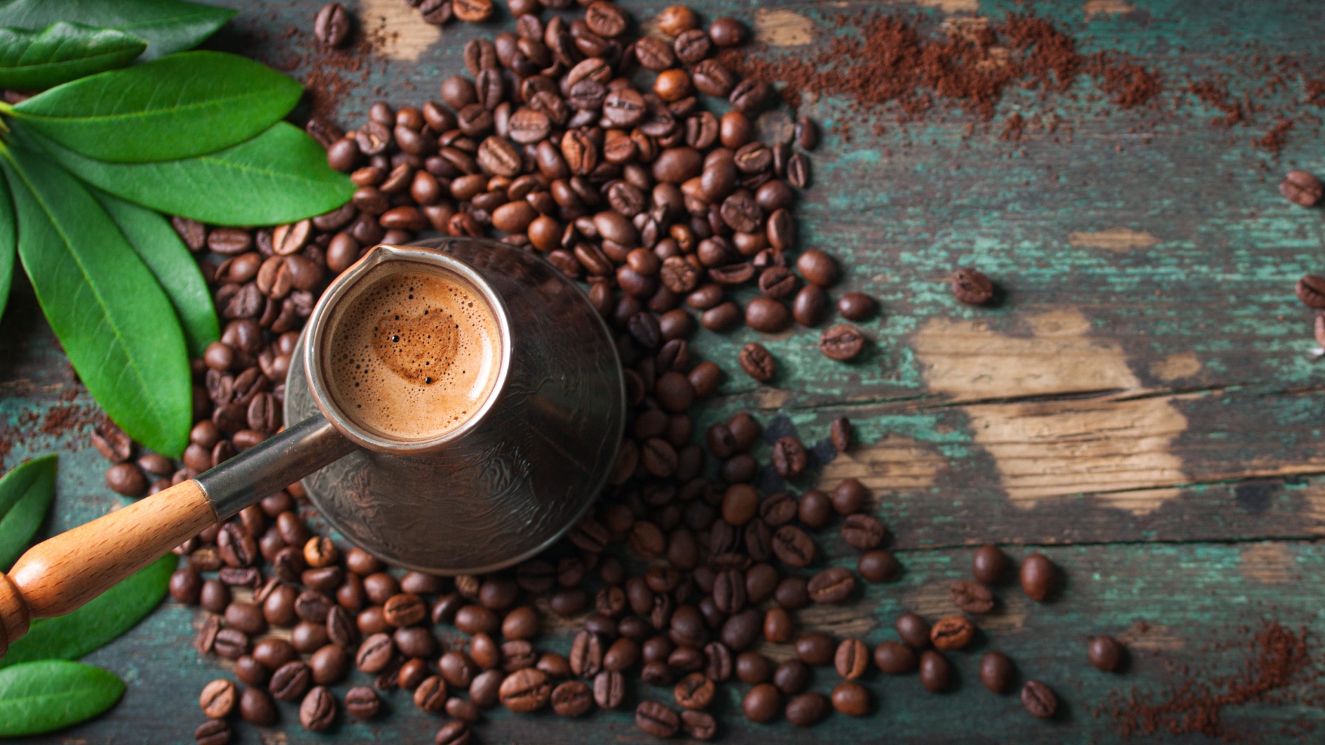 Турка с кофе на столе с зернами и зелеными листьями