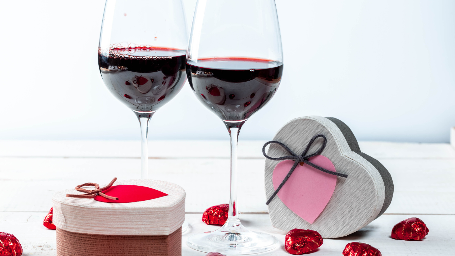 Две коробки с конфетами в форме сердца на столе с бокалами 