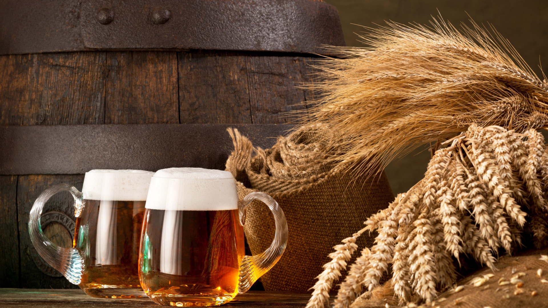 Два бокала пива на столе с колосьями пшеницы  и бочкой