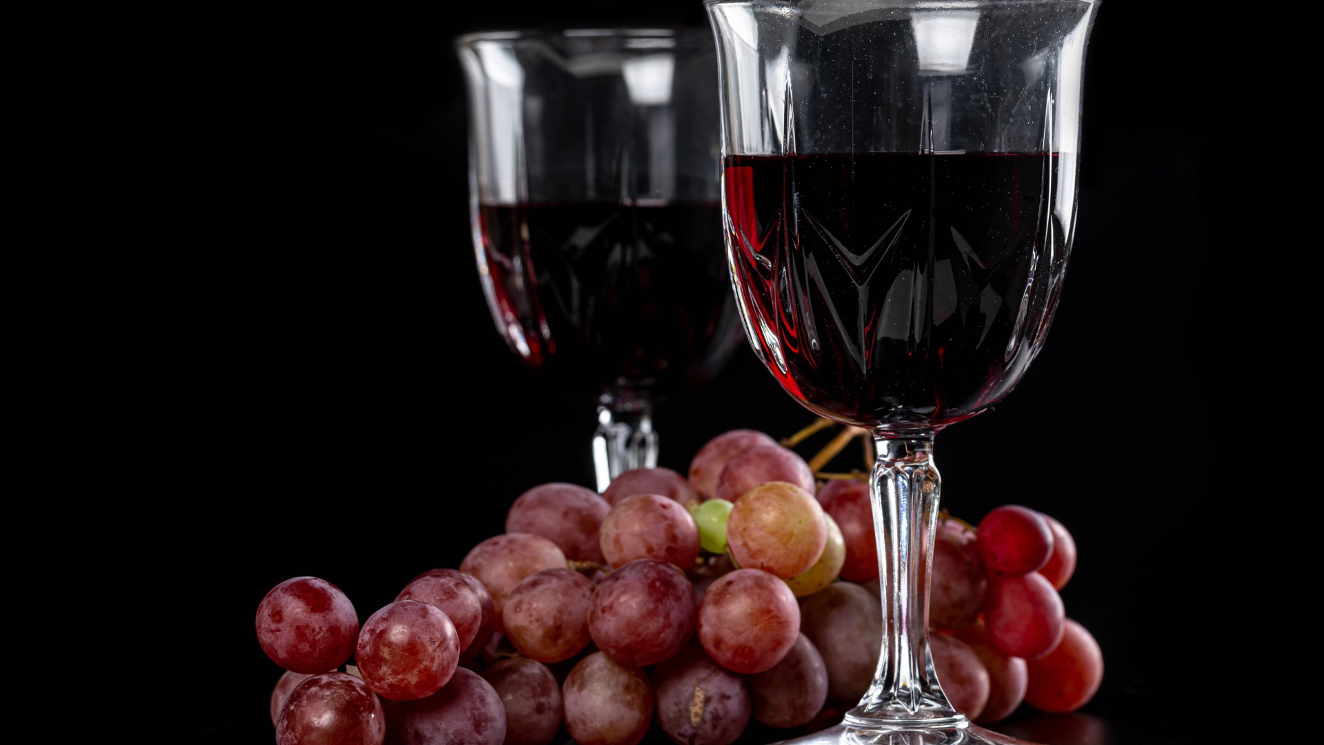Два бокала вина на черном фоне с виноградом 