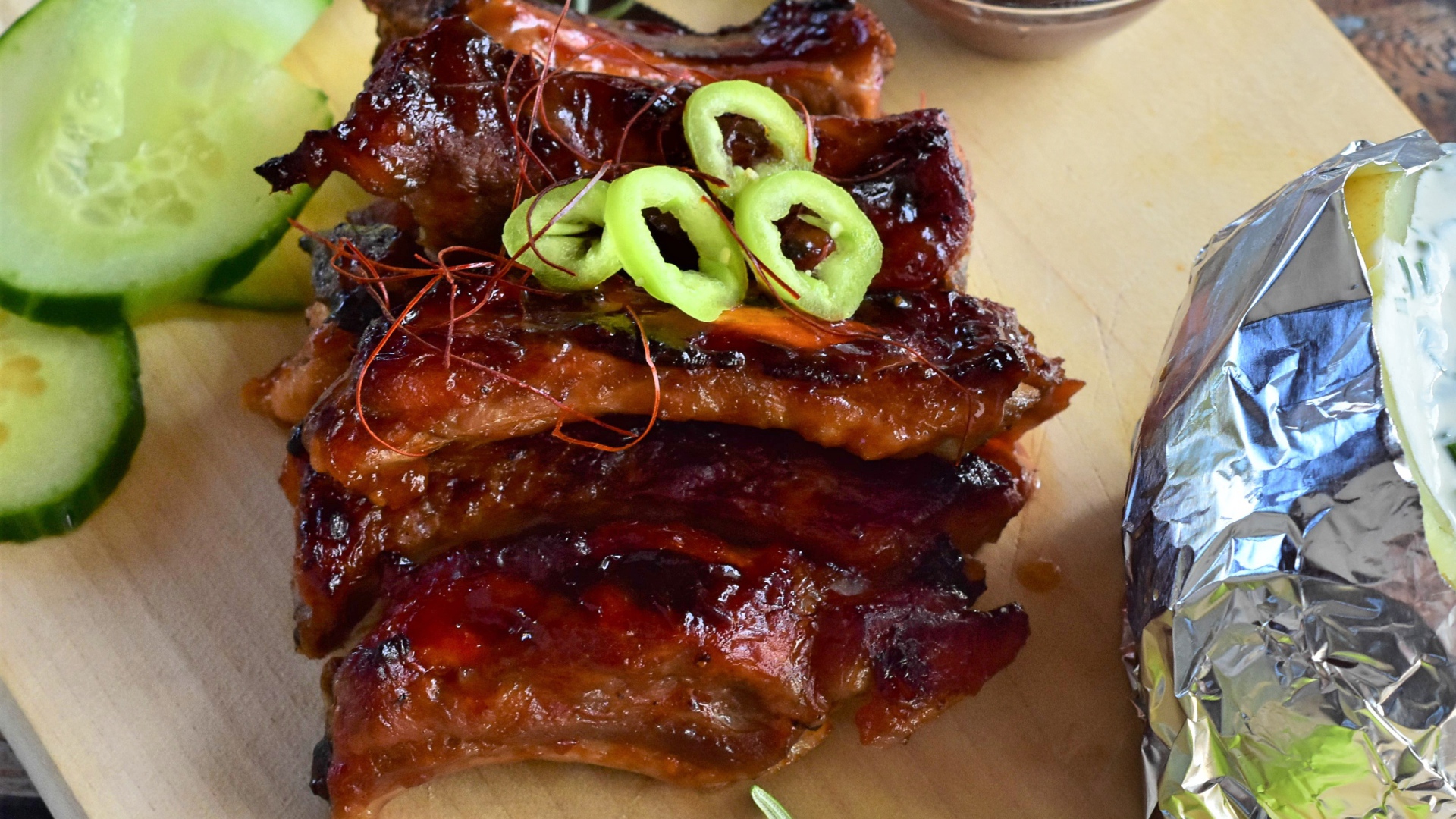 Аппетитные жареные ребрышки на столе с огурцами  и соусом 