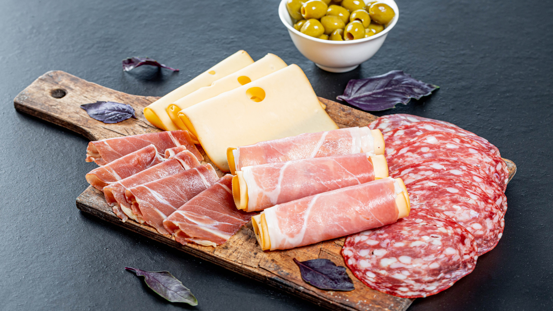 Сыр, бекон и колбаса на разделочной доске на столе с оливками