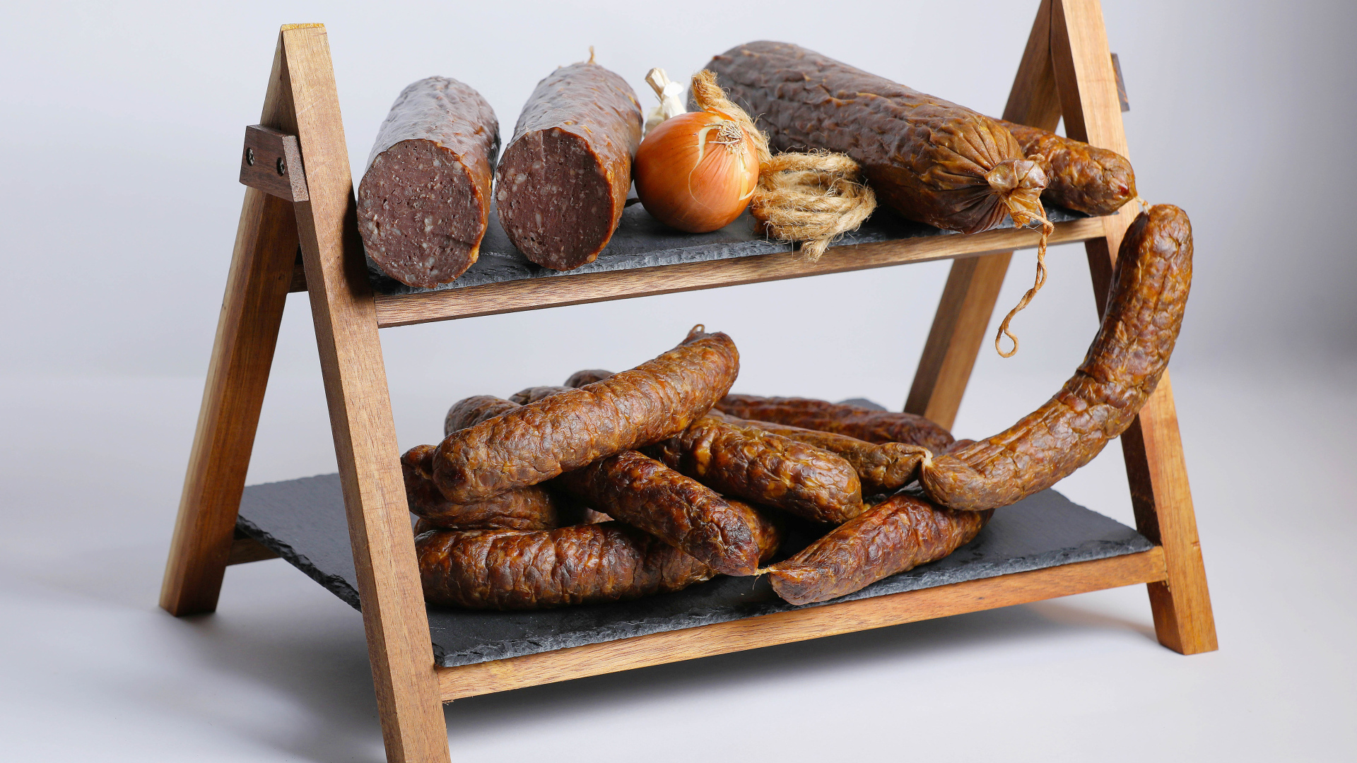Различные виды колбасы на полке с луком на сером фоне