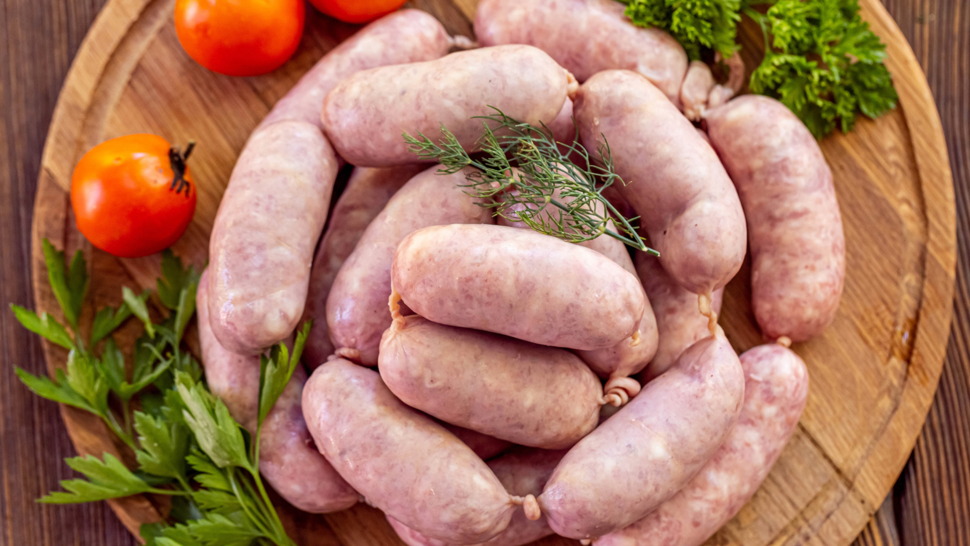 Свежие сырые домашние сардельки на доске с петрушкой и помидорами