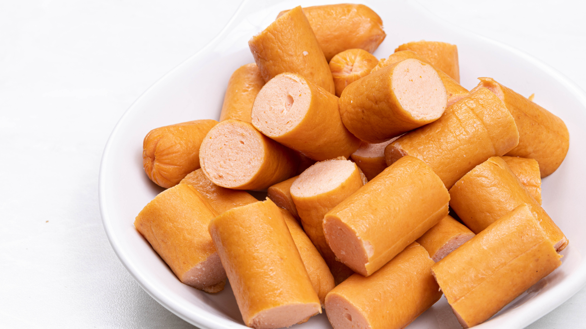 Молочные сосиски кусочками на белом фоне