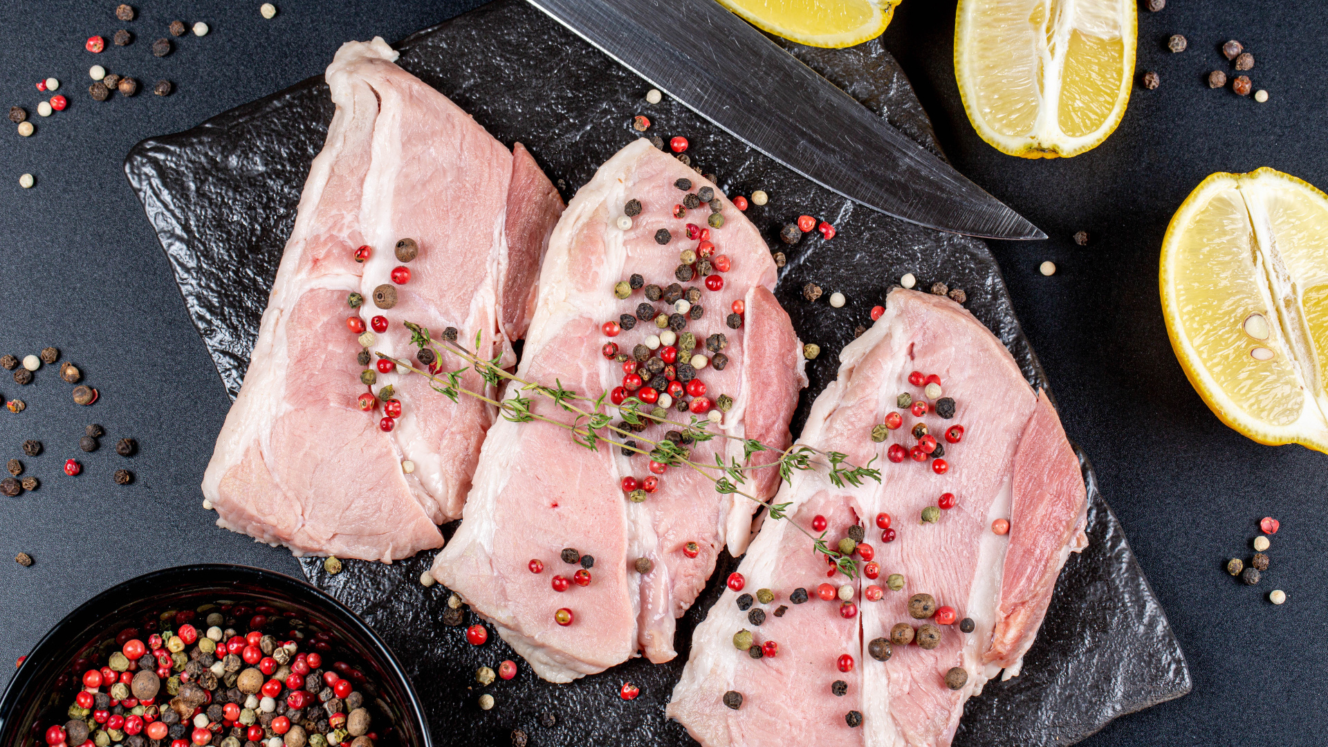 Куски свежего мяса на столе с зернами перца и лимоном