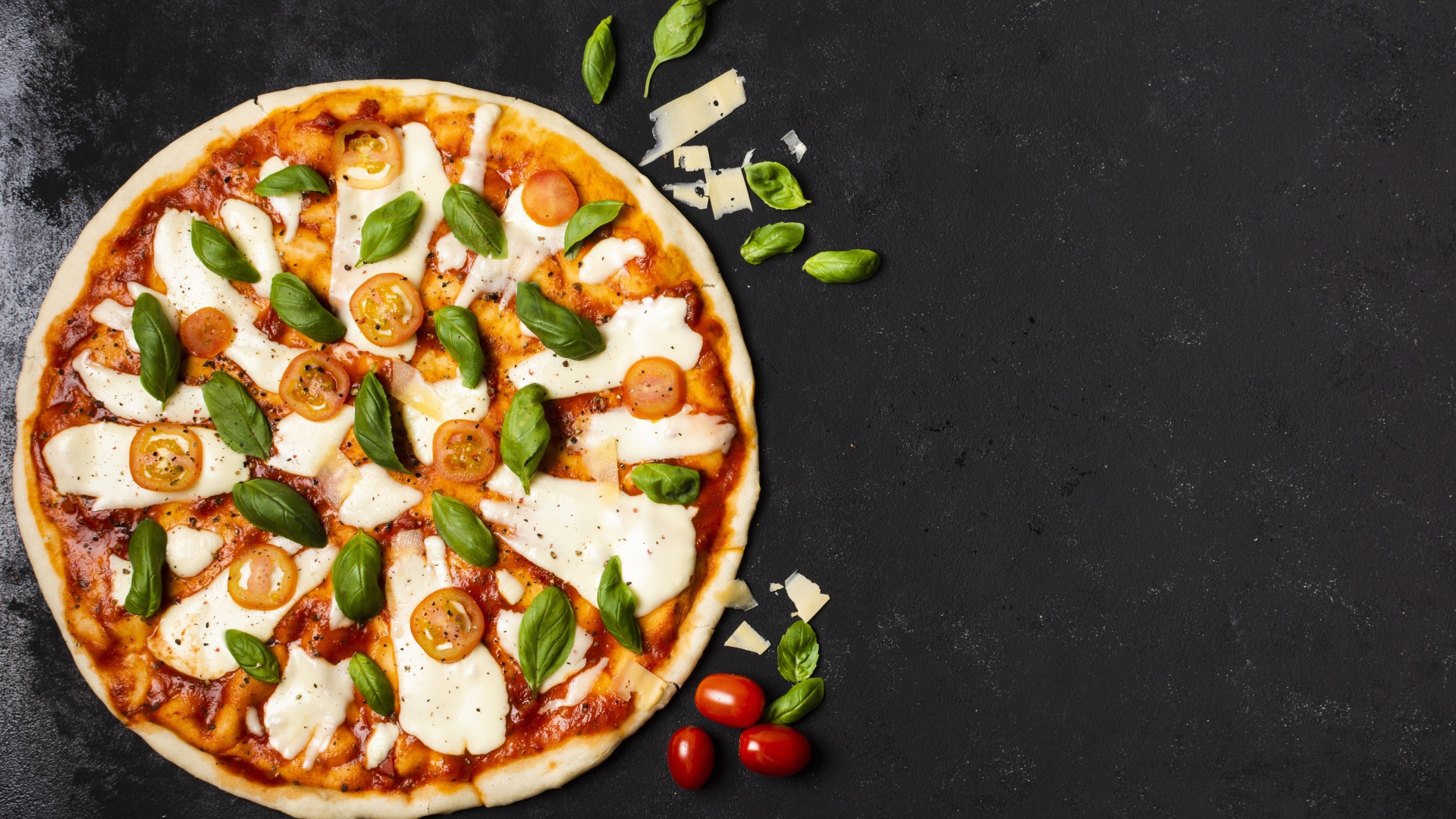 Пицца с сыром, базиликом и помидорами на черном столе 