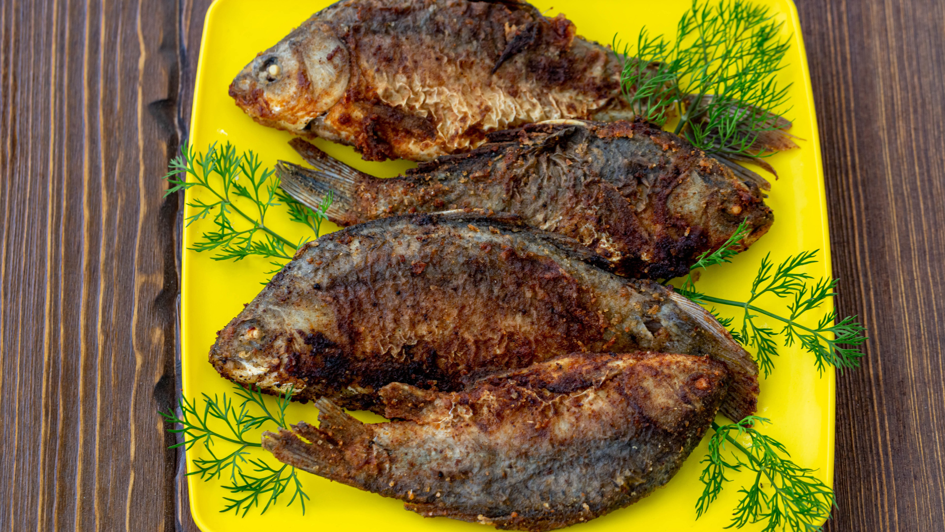 Жареные караси с укропом на желтой тарелке 