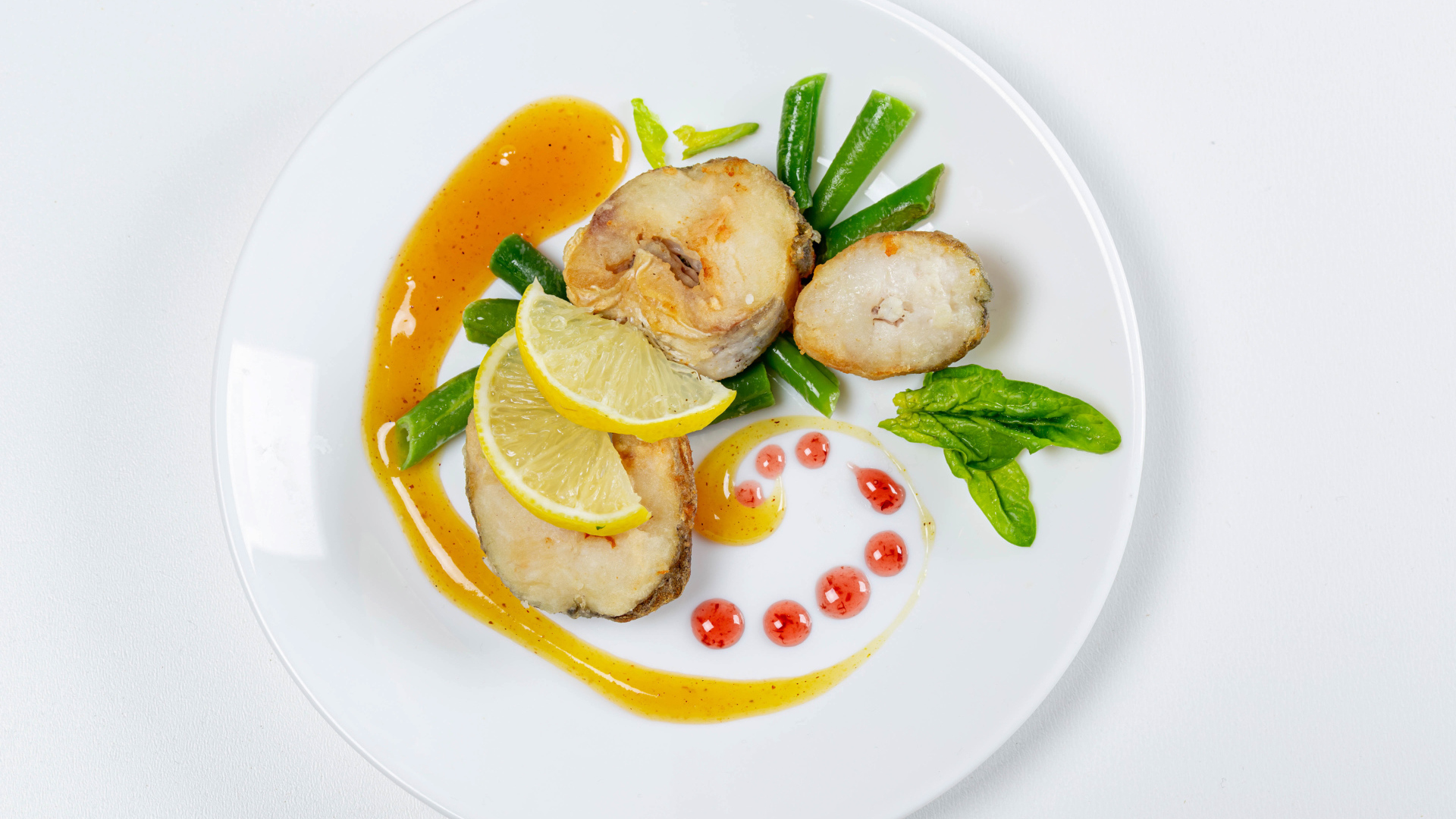 Кусочки жареной рыбы на белой тарелке с лимоном и зеленью