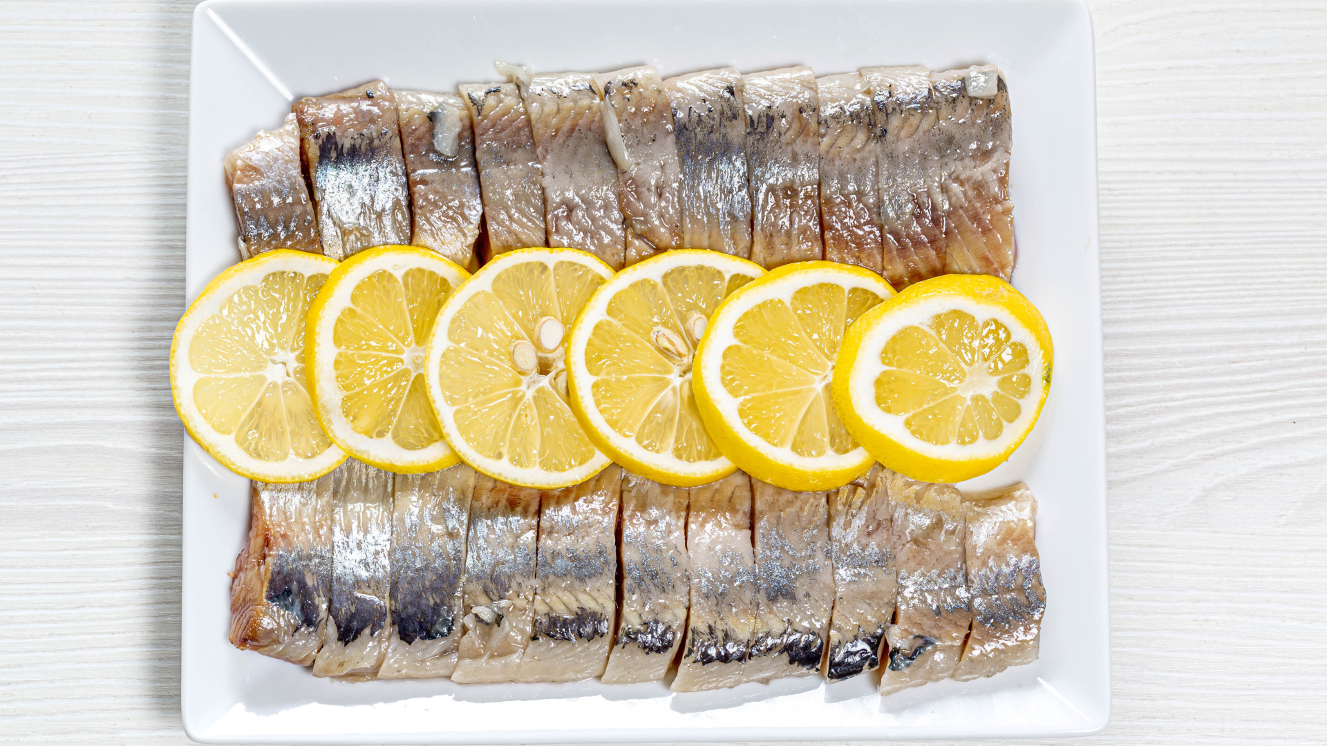 Селедка нарезанная кусочками на белой тарелке с лимоном 