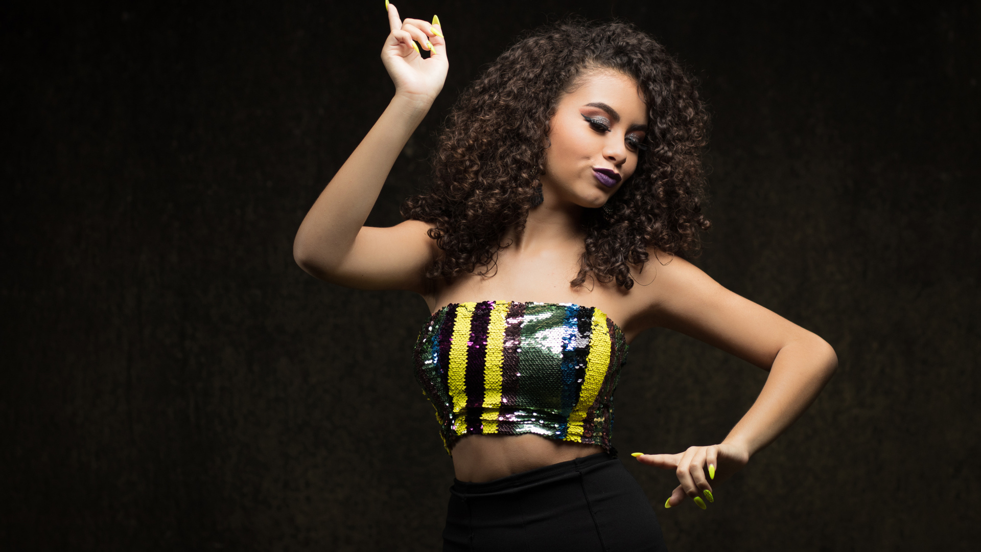 Девушка в ярком топе и черной юбке танцует у стены