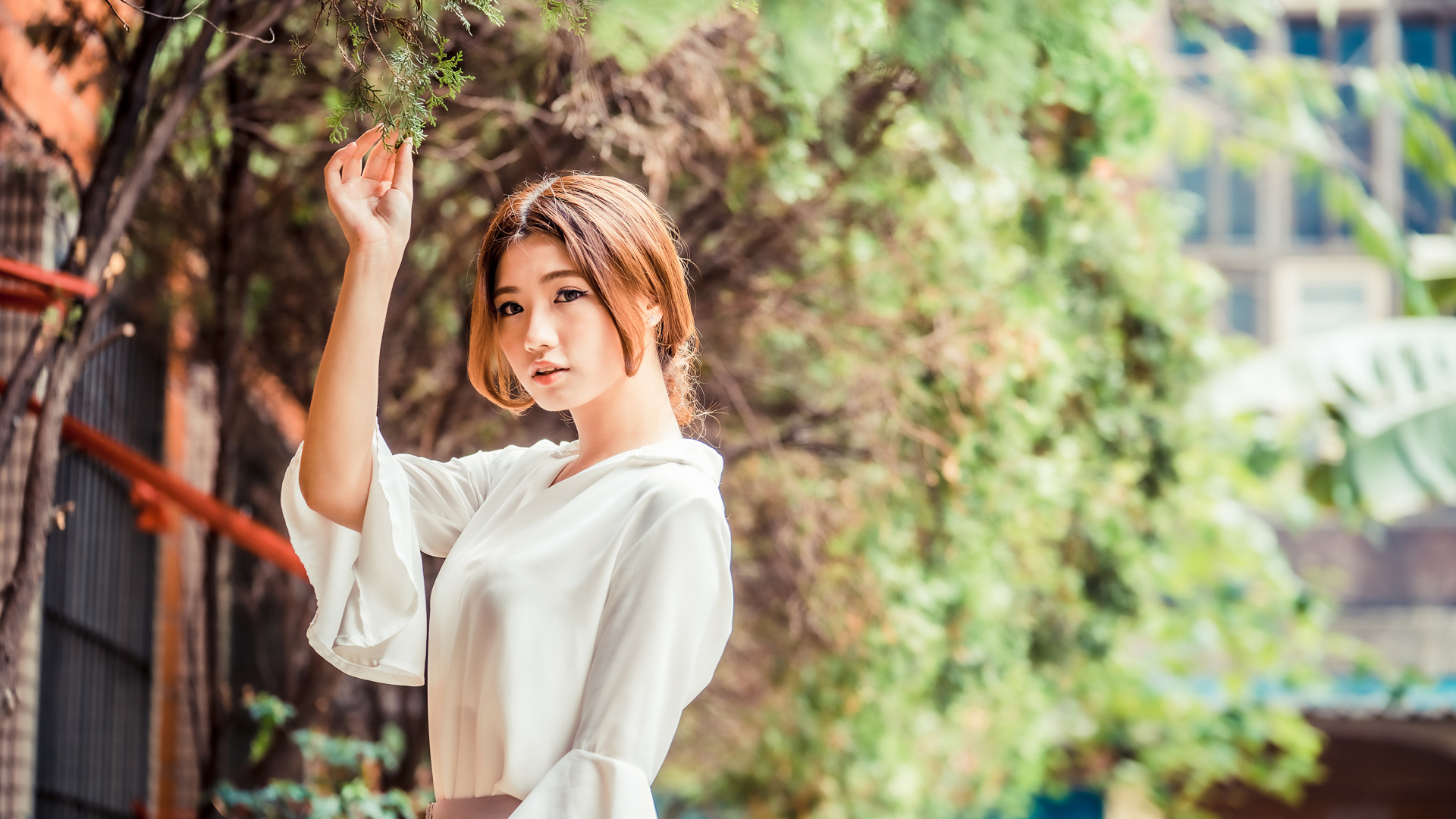 Молодая азиатка в белой блузке стоит у дерева 